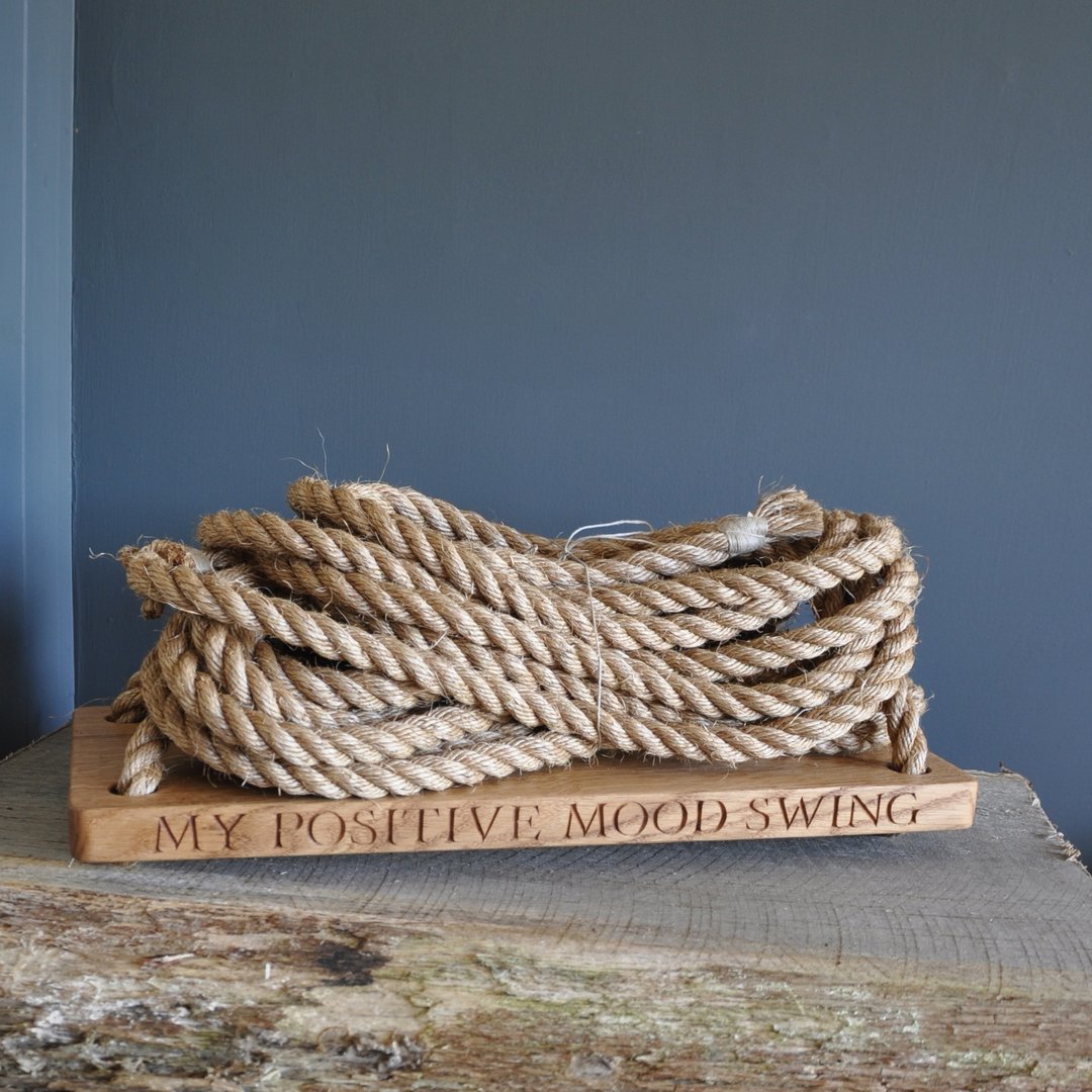 Coiled rope on an oak swing seat with 'My Positive Mood Swing' engraving against a blue wall.