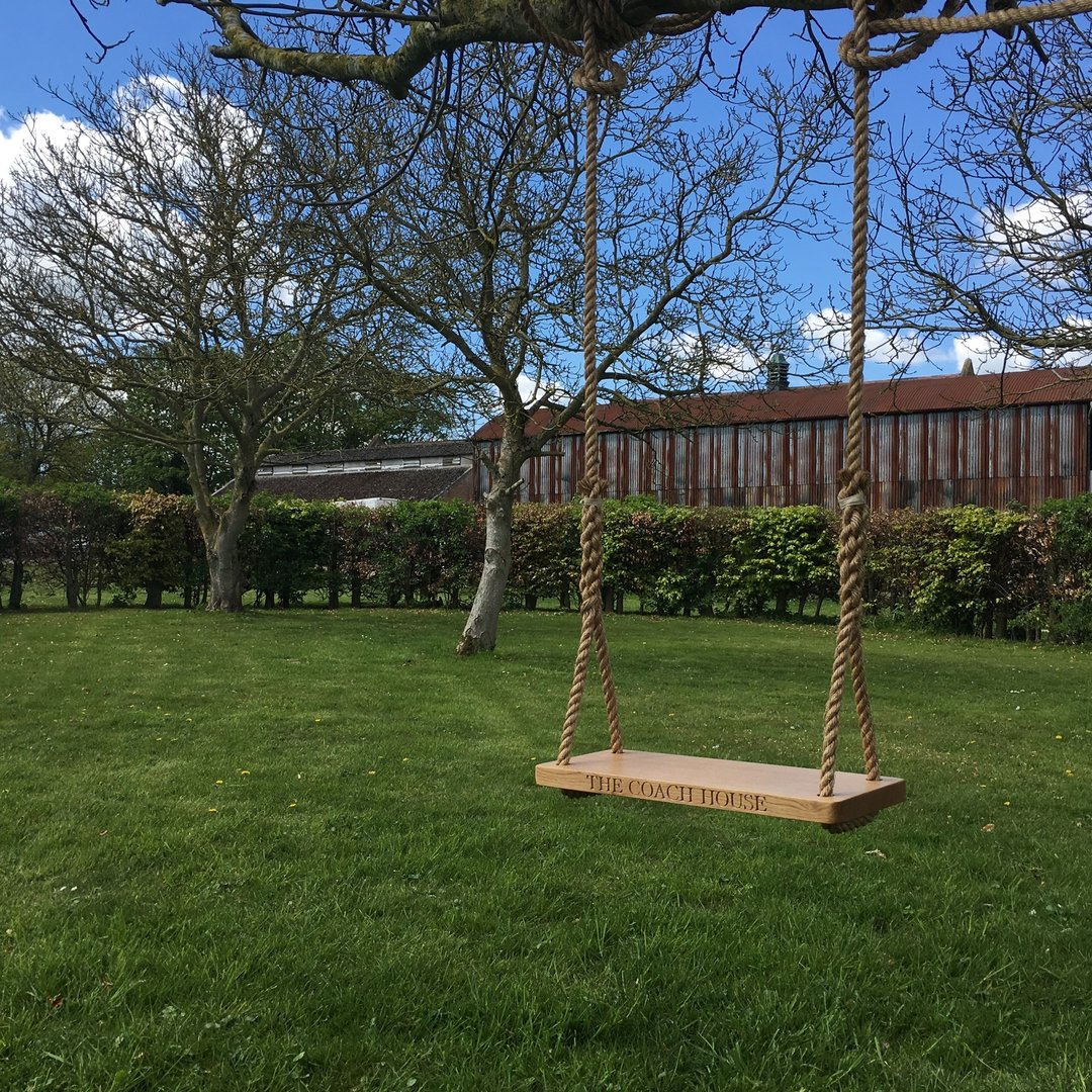 Oak and rope swing hanging from a tree in a garden with a building in the background