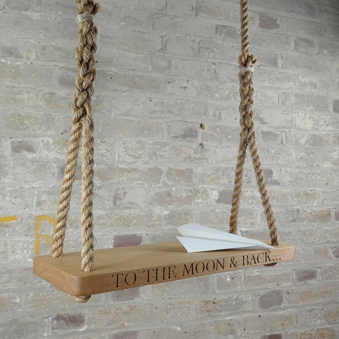 Oak and rope swing with 'To the Moon & Back' text engraved against a brick wall.