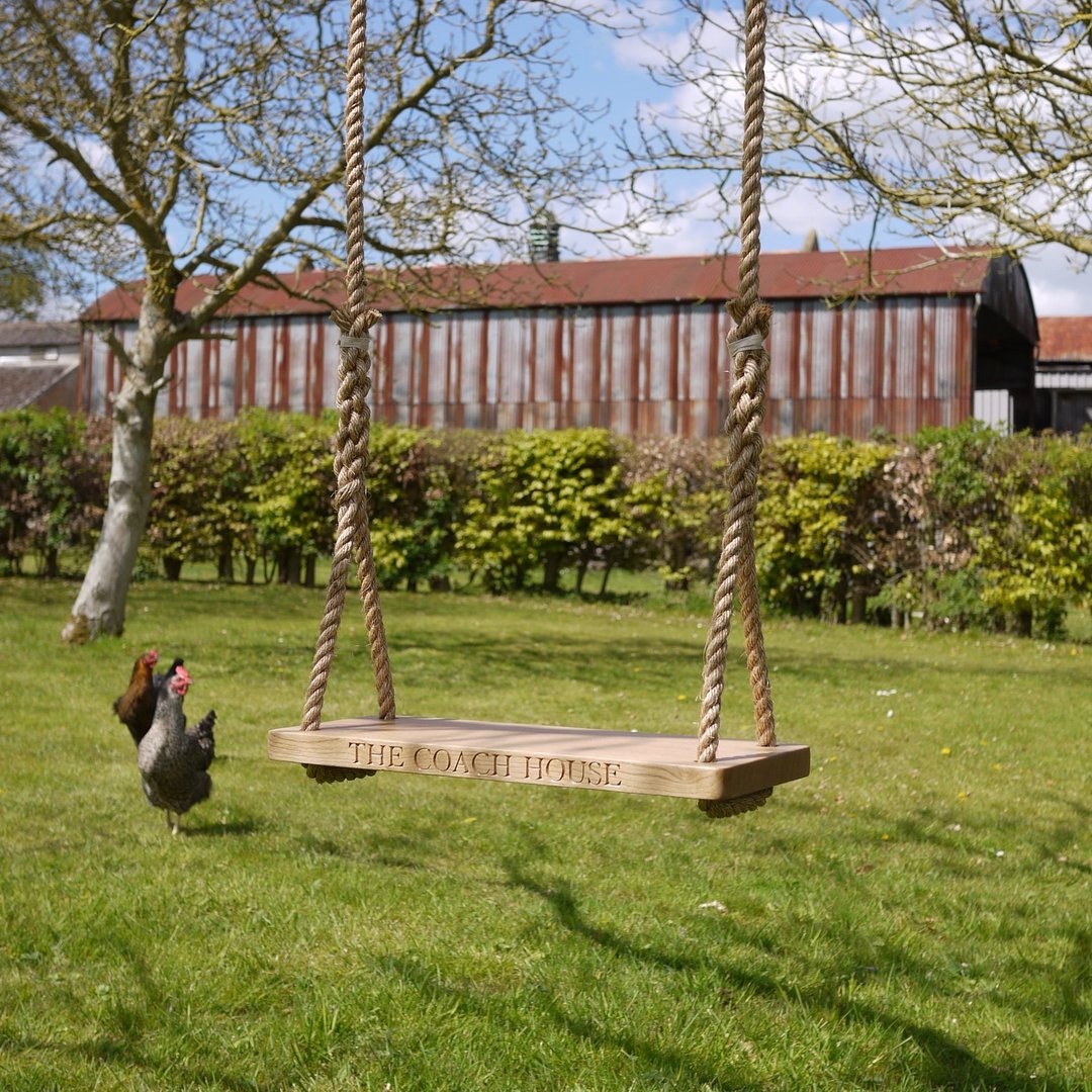 Oak and rope swing with 'The Coach House' engraving on a grassy area with a barn in the background.