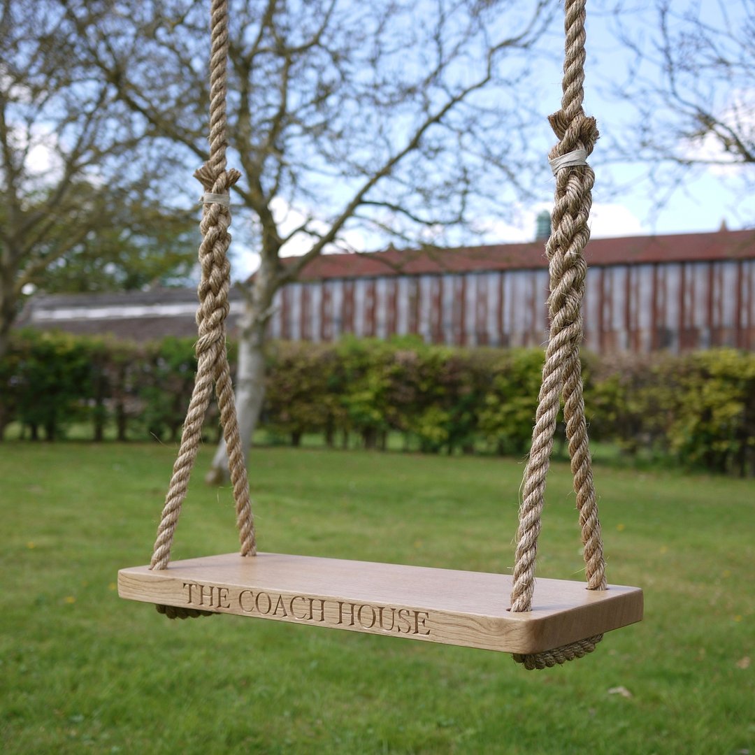 Oak and rope swing with 'The Coach House' engraving in a garden setting