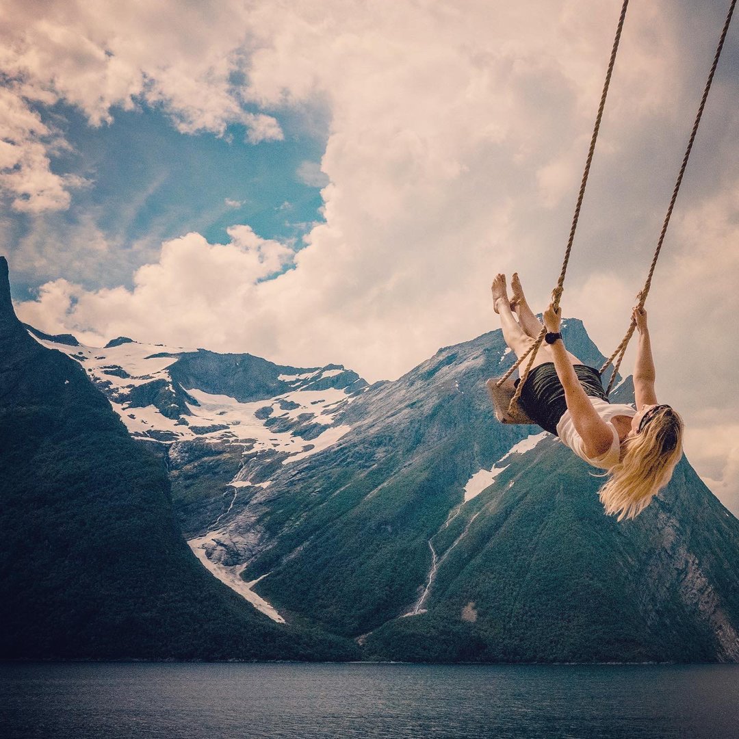 Person on an oak and rope swing with mountains and water in the background