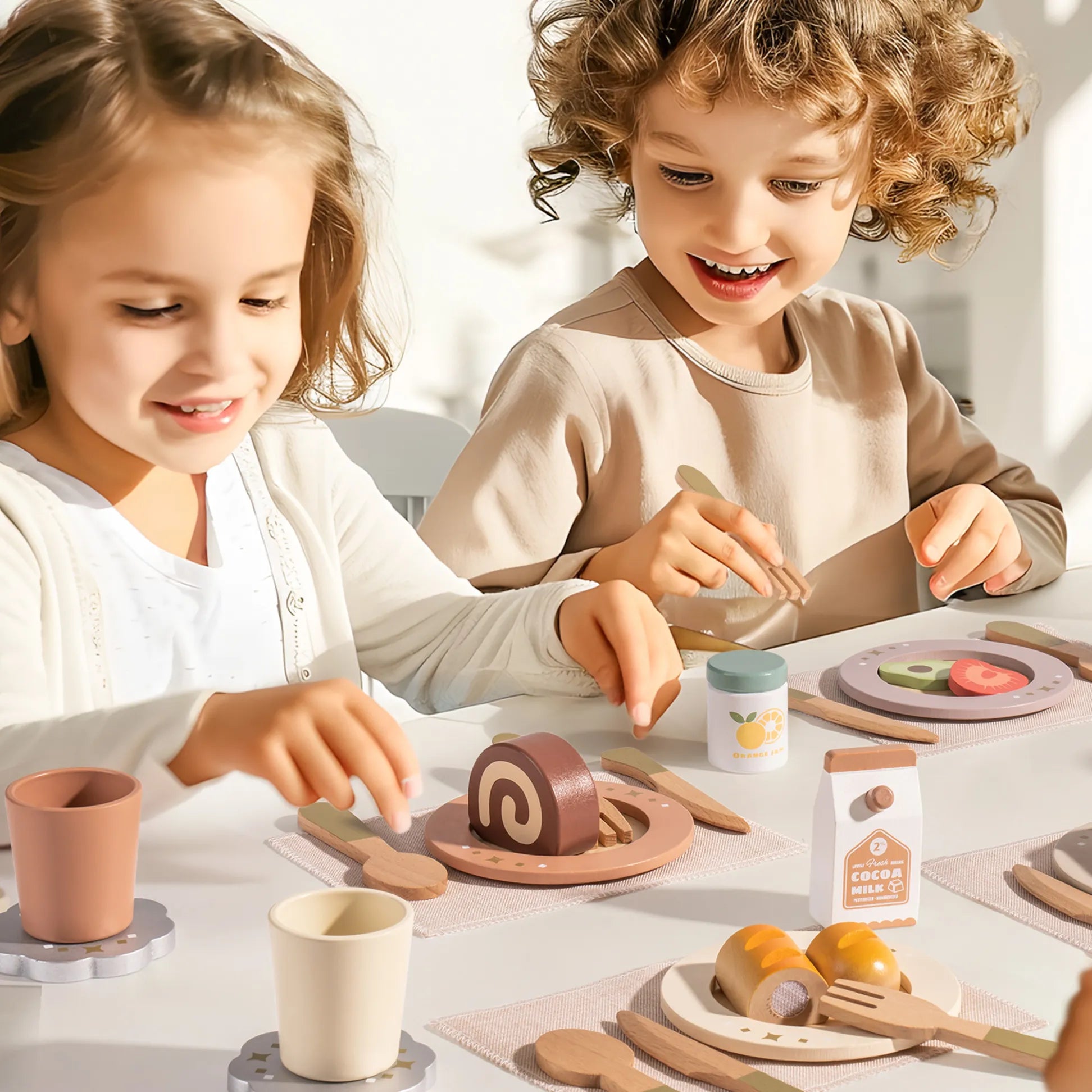 Two children playing with a toy kitchen set on a table. Wooden dinnerware play set for kids – ROBUD 29-piece set with plates, cups, and utensils with wooden play food