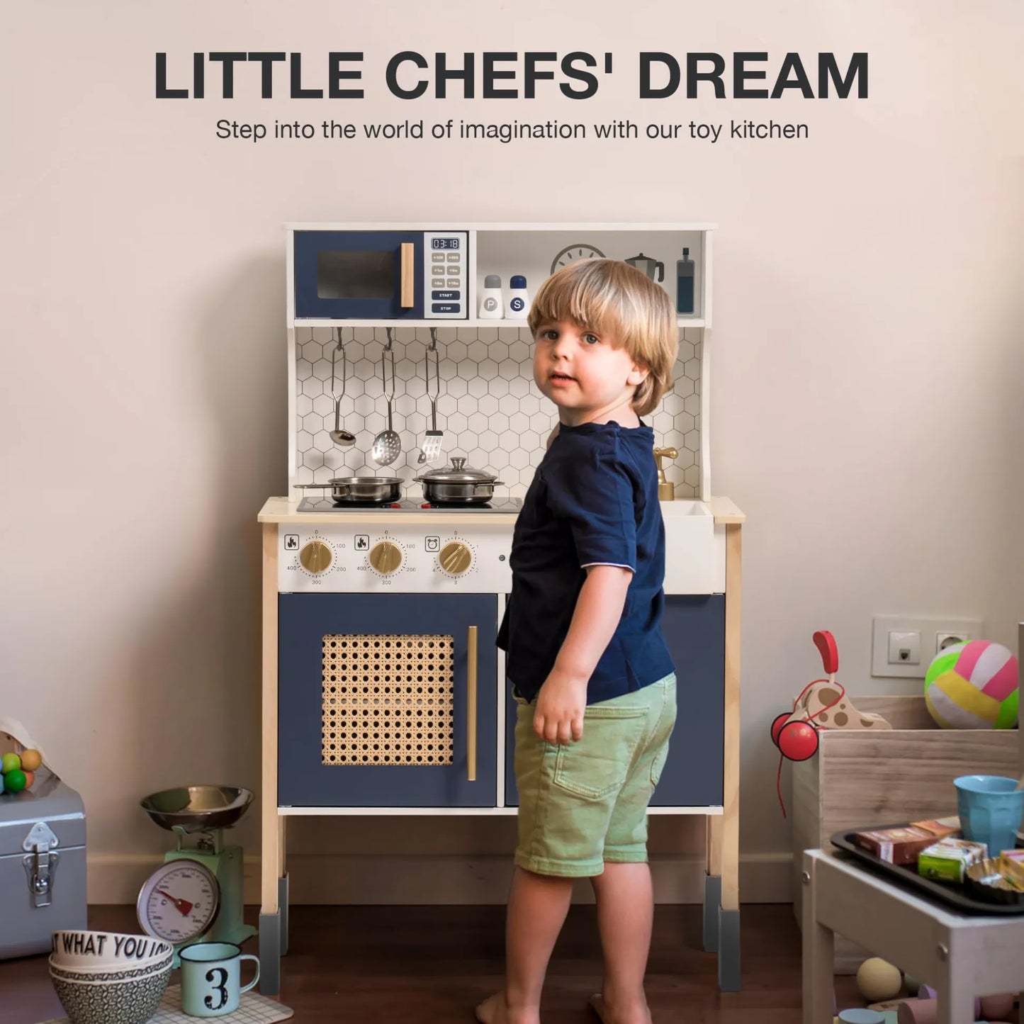 Child standing next to a toy kitchen set with various accessories on a wooden floor.