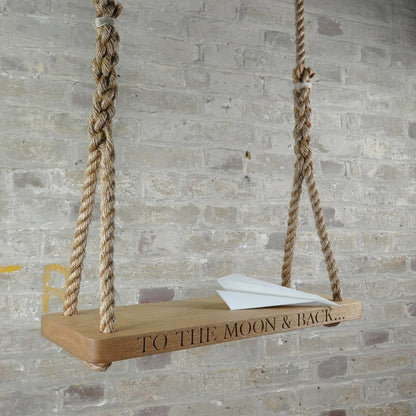 Oak and rope swing with 'To the Moon & Back' text engraved against a brick wall.